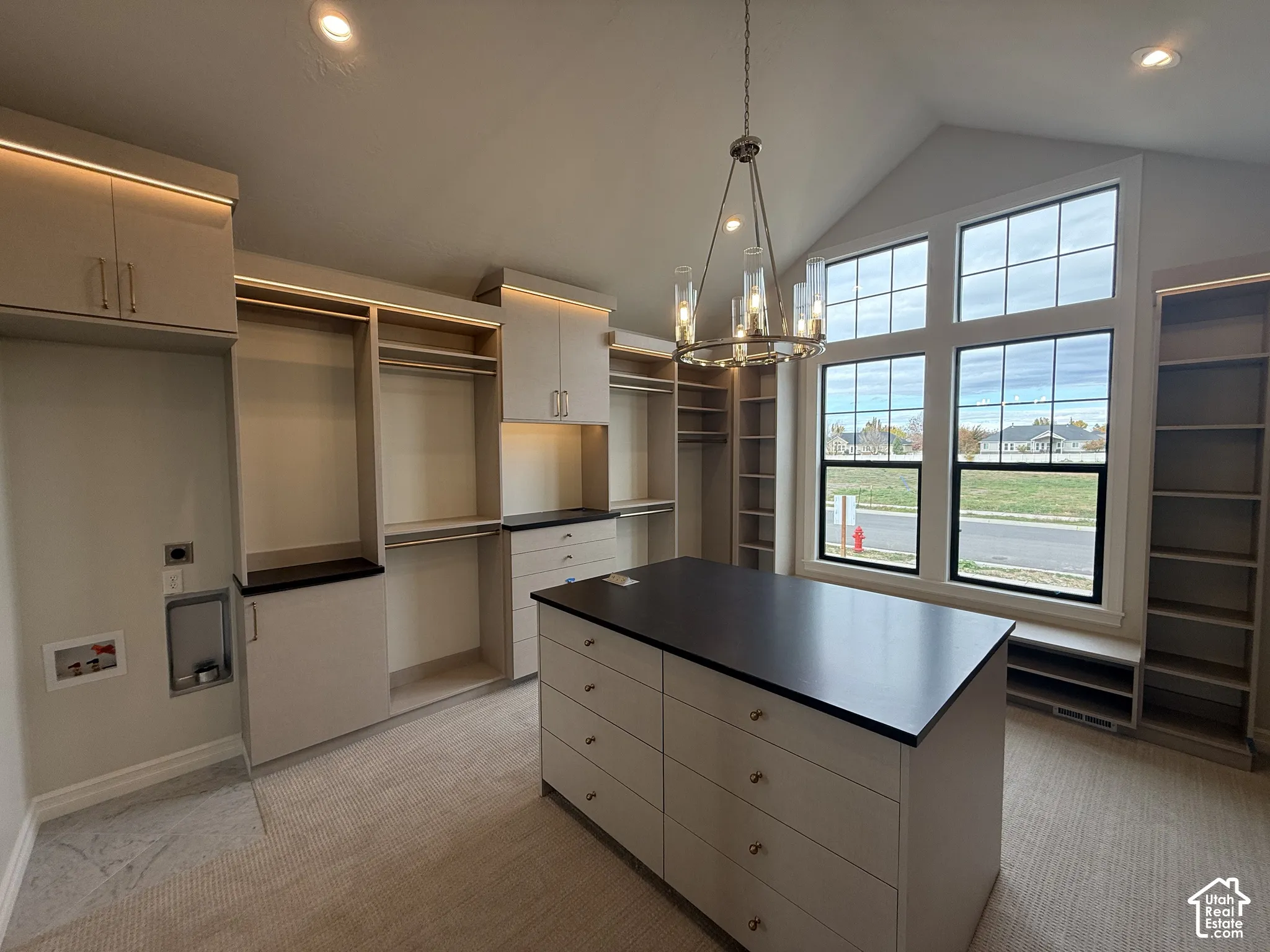 Custom built-in cabinetry with integrated lighting, a central island with a solid surface countertop, vaulted ceilings, multi-pane windows, and a multi-tiered metal chandelier