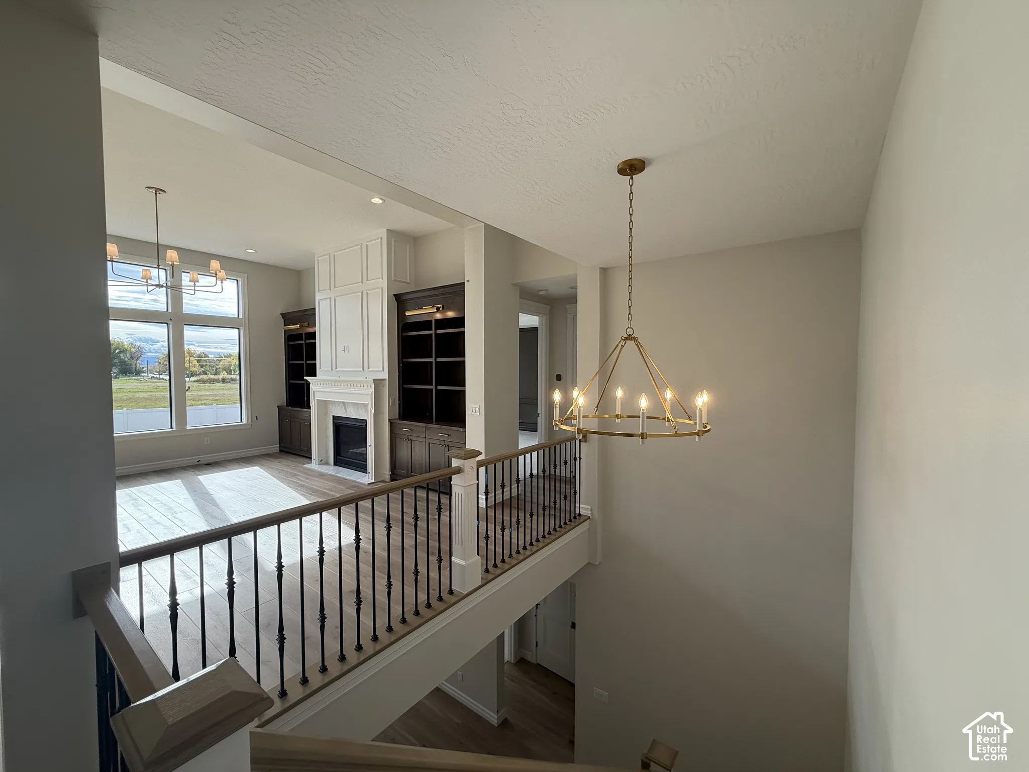 Open-concept area featuring wood-finish flooring, built-in cabinetry, a fireplace with floor-to-ceiling millwork, metal baluster railings, and multi-light pendant chandeliers