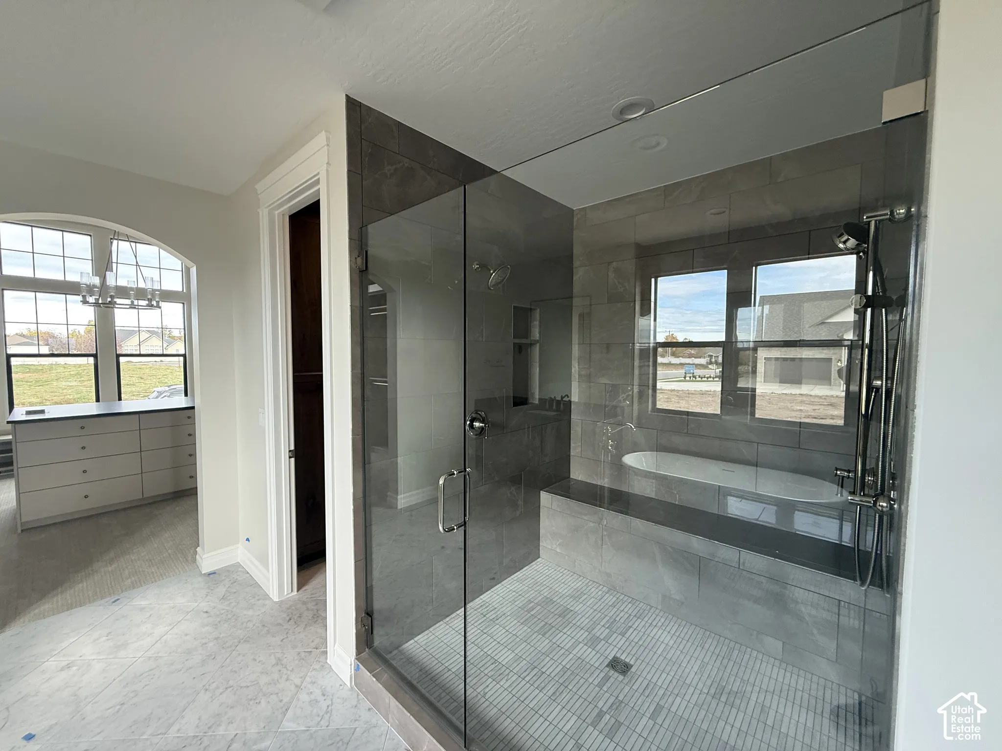 Walk-in shower with floor-to-ceiling tile, frameless glass enclosure, built-in tiled bench, and separate hand-held shower fixture