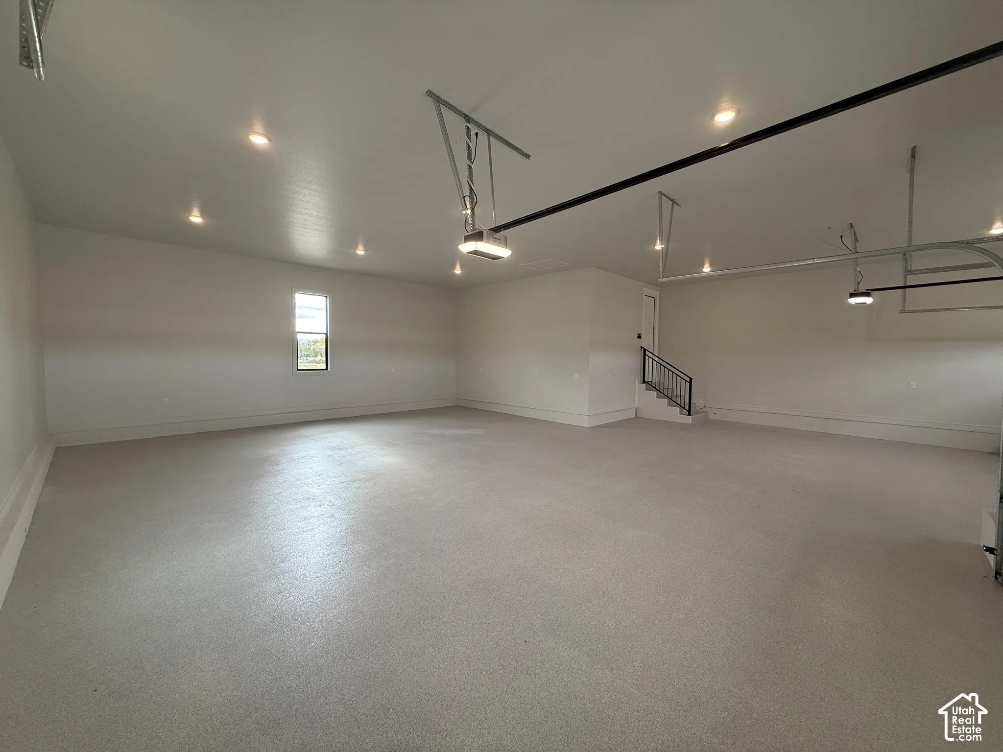 Spacious multi-car garage featuring epoxy-finished concrete flooring, recessed lighting, high ceilings, and a metal-railed staircase