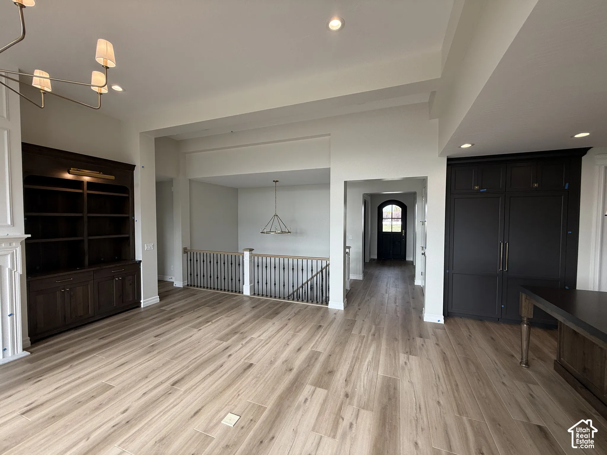Open-concept space featuring wood-finish flooring, built-in dark wood cabinetry with integrated lighting, matte black full-height cabinetry, and metal baluster railing