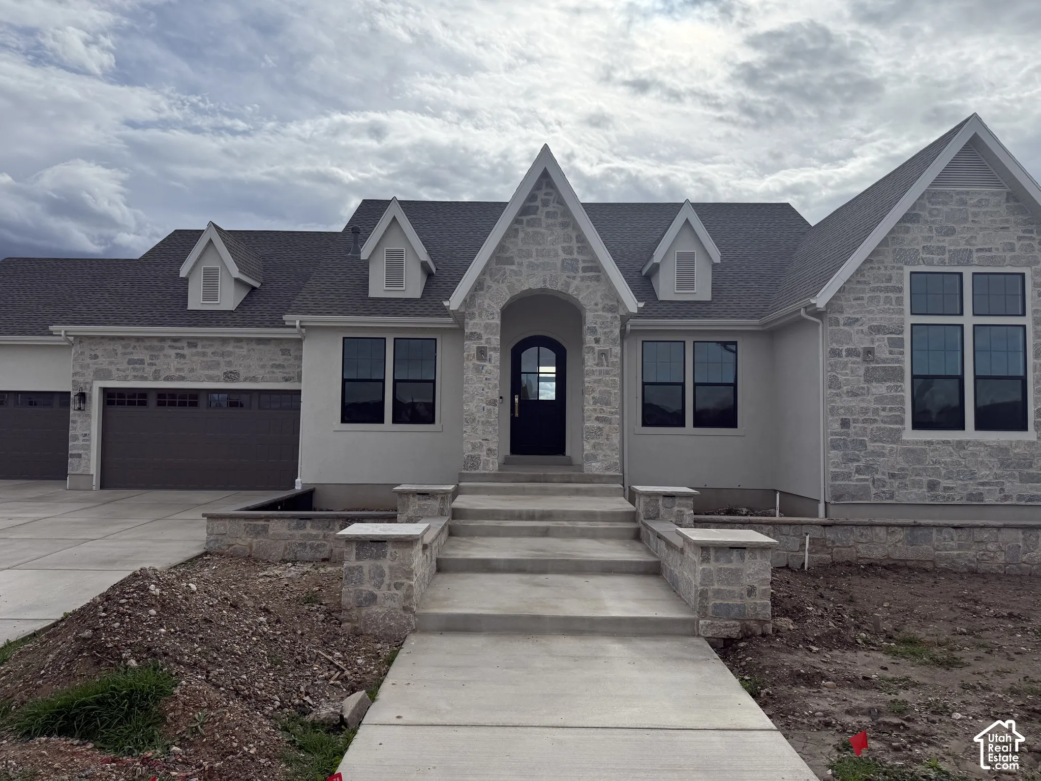 Exterior facade featuring stone veneer, multi-gabled roofline, arched entryway, and multi-car garage with concrete driveway