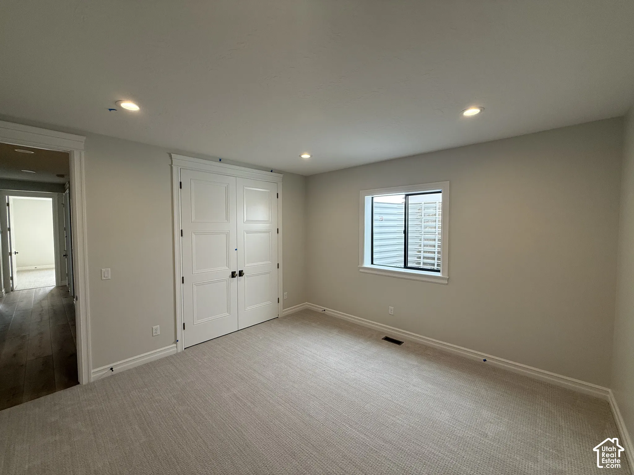 Room featuring neutral carpeting, recessed lighting, double doors with matte black hardware, and a window with a tiered light well exterior