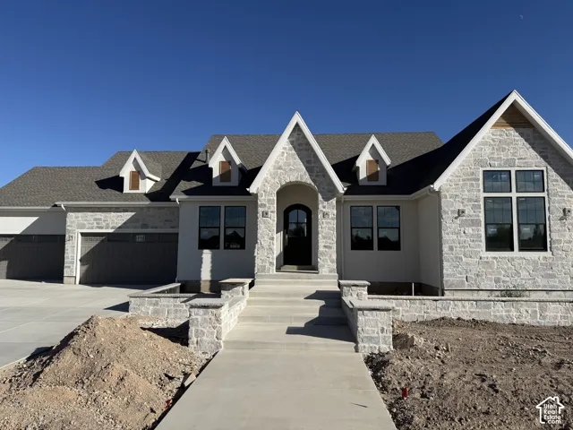 Stone facade with dormer windows, an arched entry, and a multi-car garage