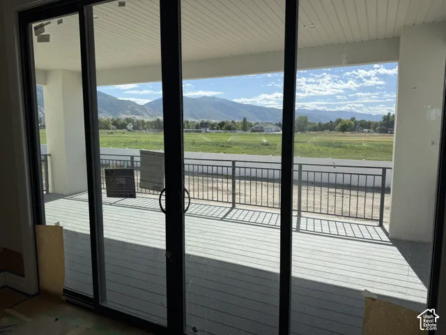 Sliding glass doors opening to a covered outdoor deck with composite decking, black metal railings, and mountain scenery