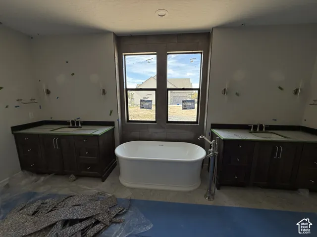 Freestanding bathtub with floor-mounted faucet, dual vanities with dark wood cabinetry, and recessed ceiling lighting
