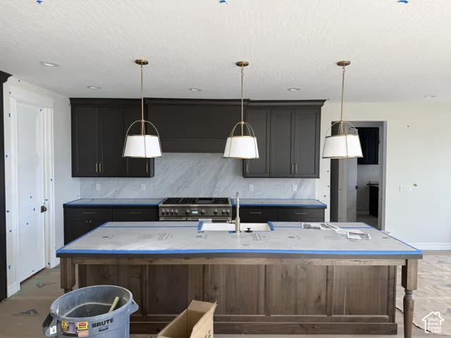 Kitchen featuring dark-toned cabinetry, light-toned backsplash, stainless steel range, and a wood-finish island with integrated sink