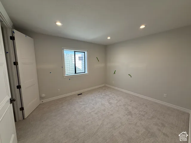 Recessed lighting illuminates the space, featuring a window with trim, a paneled door, and neutral-toned carpet