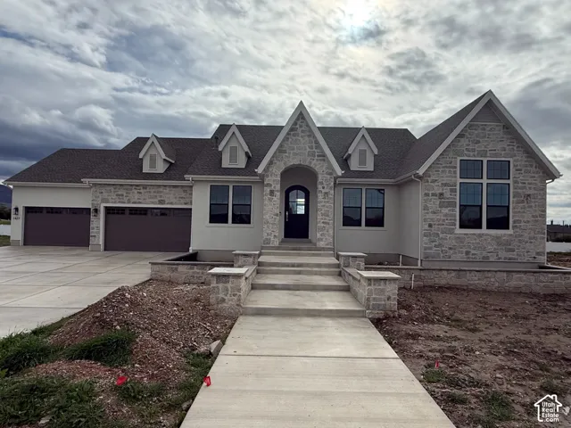 Exterior featuring stone and stucco facade, triple-gabled roofline, three-car garage, and concrete walkway with stone-capped masonry pillars