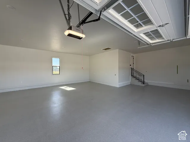 Attached garage with finished flooring, automatic garage door opener, window, and interior access stairs with wrought iron railing