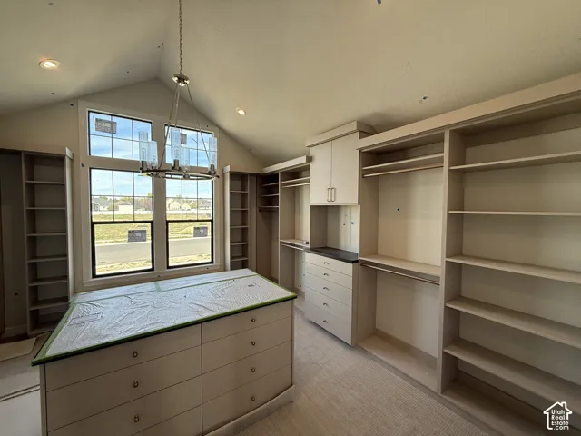 Vaulted ceiling with a contemporary chandelier, multiple built-in shelving units, built-in drawer storage, and a central island with integrated drawers