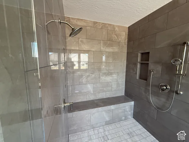 Walk-in shower with tiled walls, built-in bench, recessed shelf, and glass enclosure