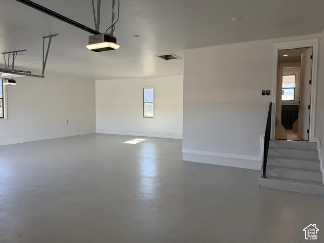 Spacious garage featuring a light-toned floor, multiple windows, and a staircase leading to an interior space