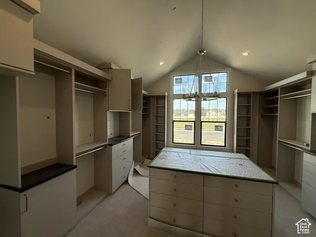 Vaulted ceiling with an elegant chandelier, built-in cabinetry with ample storage, central island with drawers, large window, and recessed lighting