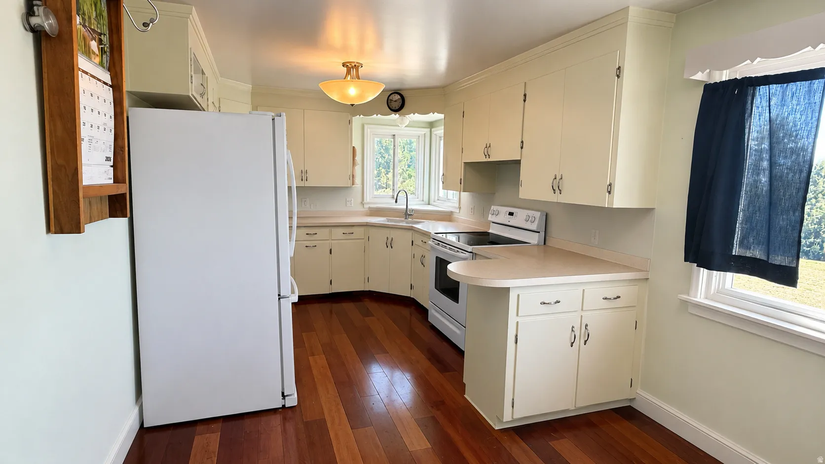 Corner kitchen featuring white cabinetry, light countertops, wood-finish flooring, a white electric range, and a bay window