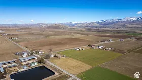 Expansive agricultural landscape featuring varied fields, scattered farm structures, a prominent water retention pond, and distant snow-capped mountains