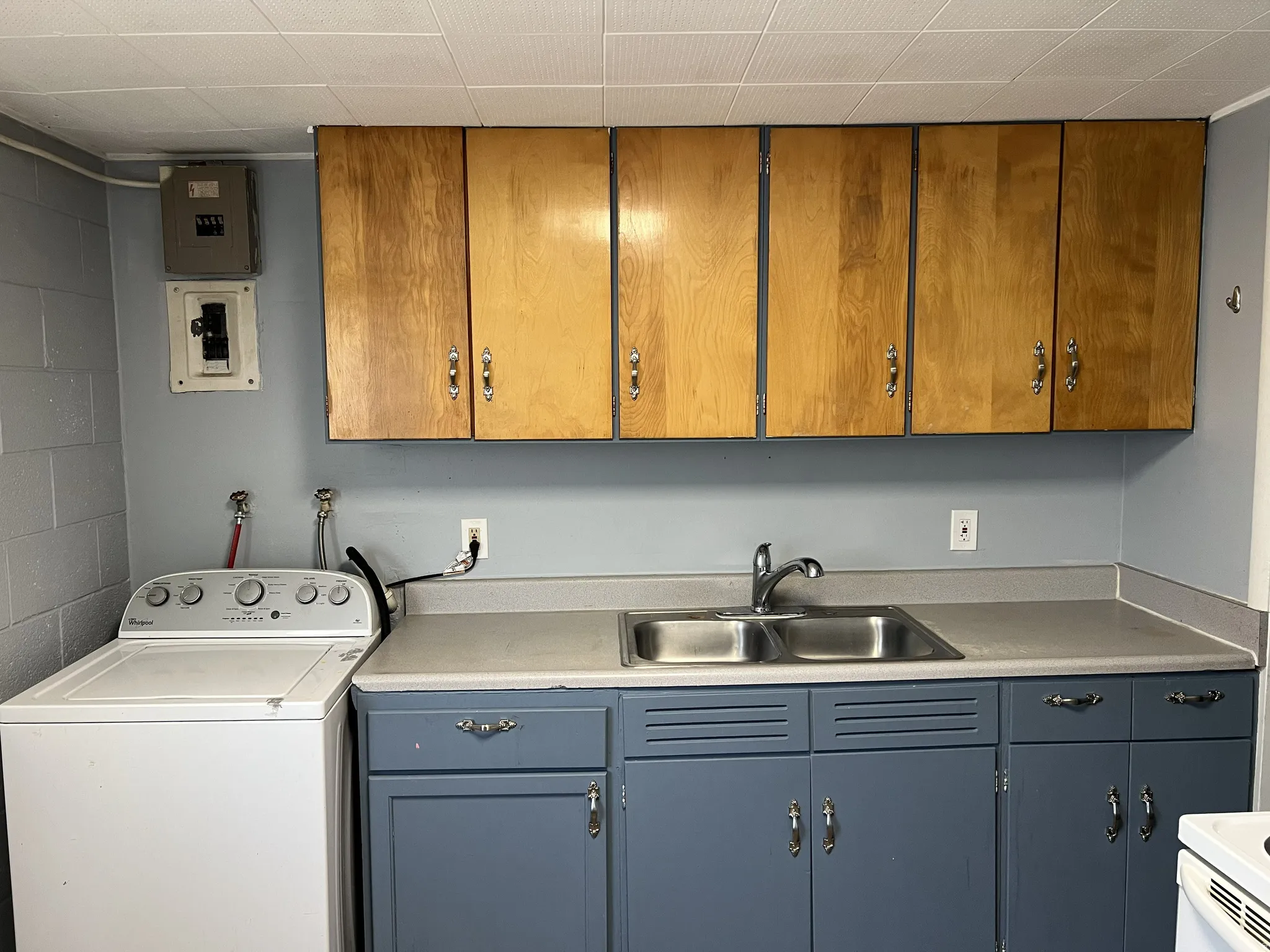 Utility area featuring a double basin stainless steel sink, wood-finish upper cabinetry, and blue painted lower cabinetry