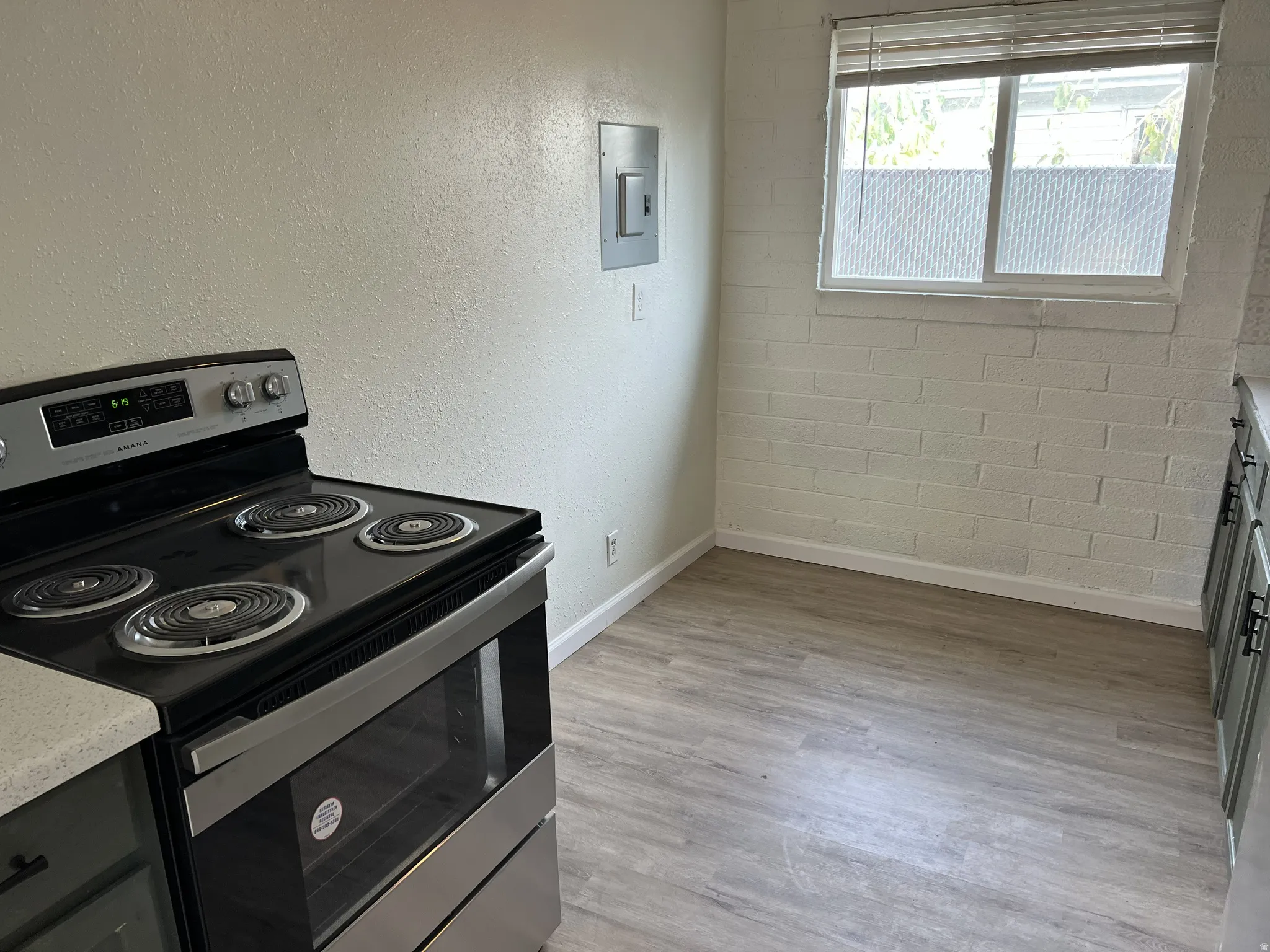 Stainless steel electric range with four burners, wood-finish flooring, and a window with blinds