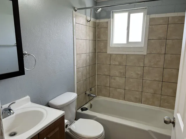 Bathroom featuring a ceramic tile bath surround, a white window, a built-in bathtub, a toilet, and a vanity with a sink