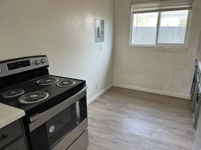 Stainless steel electric range with four burners, wood-finish flooring, and a window with blinds