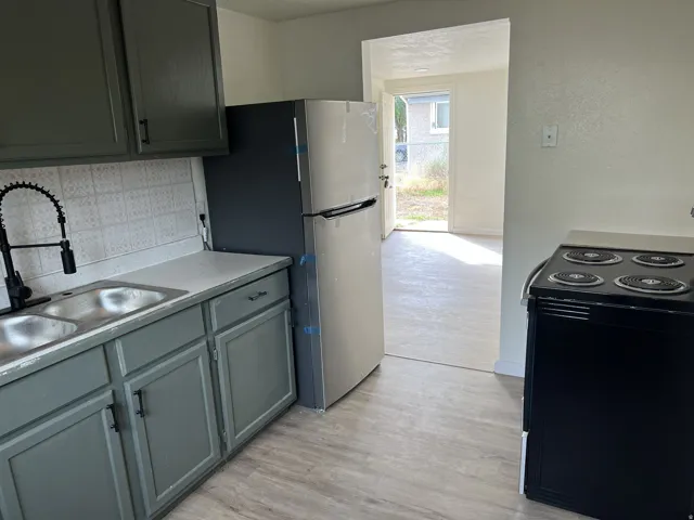 Kitchen featuring grey cabinetry, dual basin stainless steel sink with a matte black faucet, and light-toned countertops