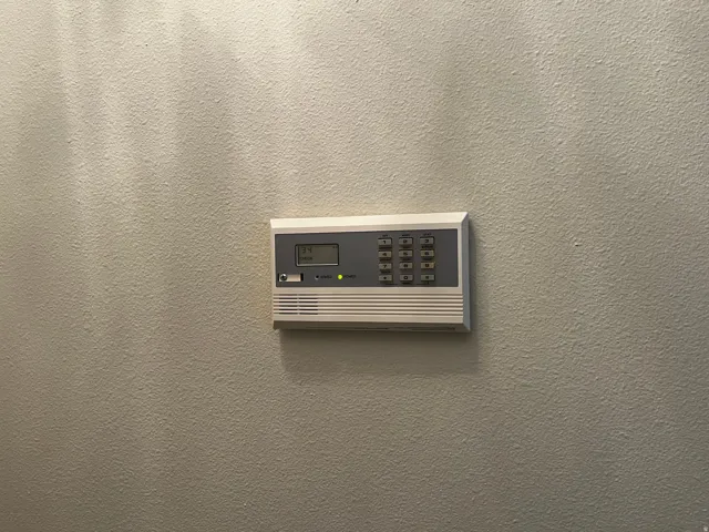 Wall-mounted security system keypad with a digital display and push-button controls, integrated into a textured wall