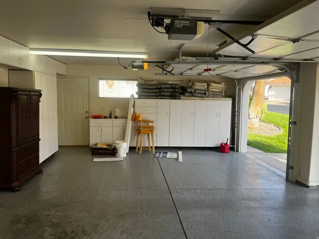 Garage featuring extensive white cabinetry, a utility sink, and durable concrete flooring