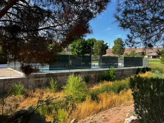Tennis courts featuring light blue surfaces, dark green fencing, and perimeter lighting