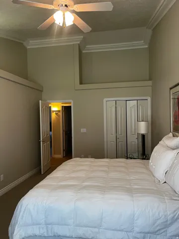 Carpeted room featuring a ceiling fan with integrated lighting, crown molding, and bi-fold closet doors