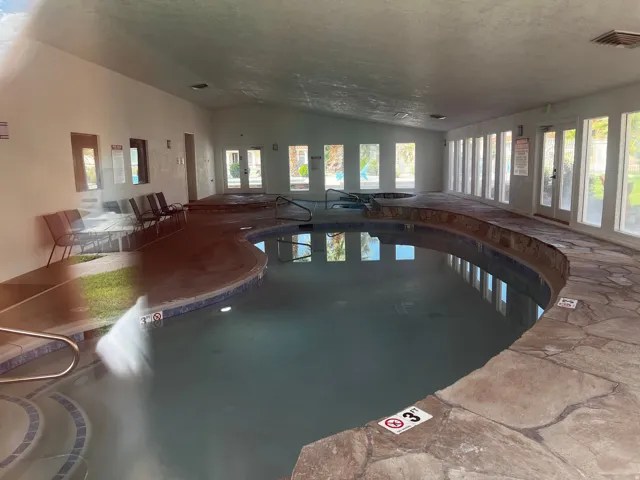 Indoor aquatic facility featuring a free-form pool, two integrated hot tubs, and stone-finish decking
