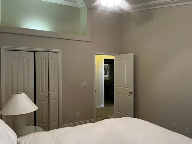 Bedroom featuring an elevated architectural shelf with accent lighting, crown molding, double bi-fold closet doors, and a ceiling fan