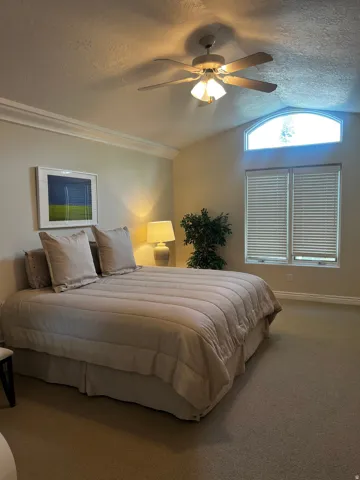 Vaulted ceiling featuring a ceiling fan with integrated lighting, crown molding, and an arched transom window