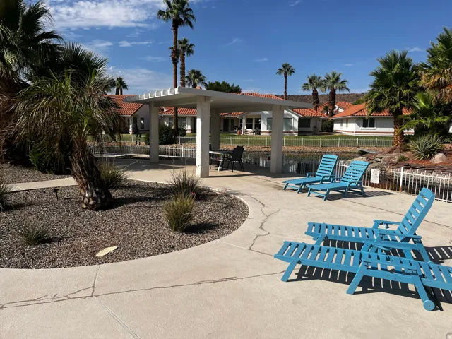 Outdoor patio featuring a white pergola, concrete paving, and a rock garden with palm trees