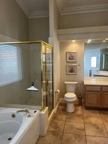 Bathroom featuring an integrated bathtub, a glass-enclosed shower with gold-finish trim, a toilet, a vanity with a light wood-finish cabinet, and tile flooring