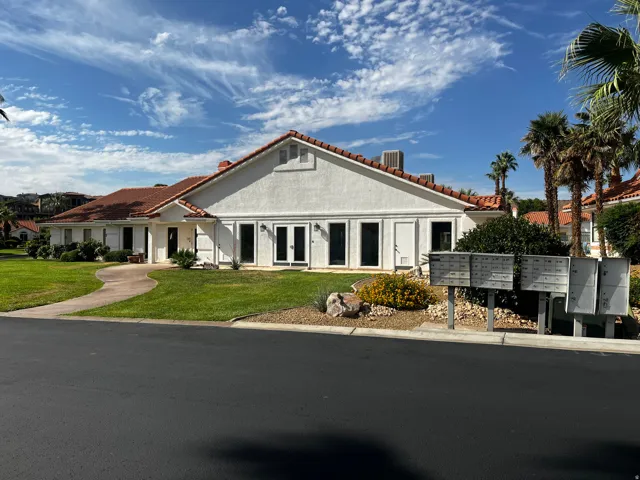 White stucco exterior featuring a red tile roof, multiple double-paned windows, a manicured lawn, mature landscaping, and a paved walkway