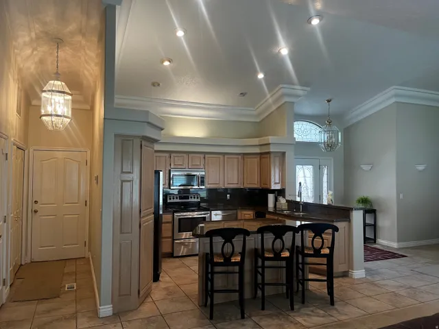 Kitchen featuring light wood cabinetry, stainless steel appliances, dark countertops, and a breakfast bar