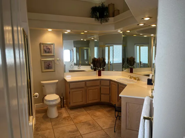 Bathroom featuring tile flooring, a built-in vanity with light-tone cabinetry, a dual-sink setup with brass-tone fixtures, and a large wall-mounted mirror with integrated lighting