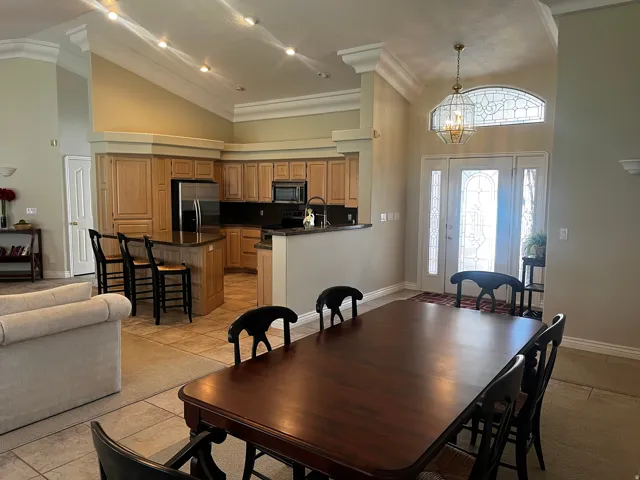 Open-concept kitchen and dining area featuring vaulted ceilings with recessed lighting, light-finish cabinetry, a central island with bar seating, and a dual-door entry with decorative glass