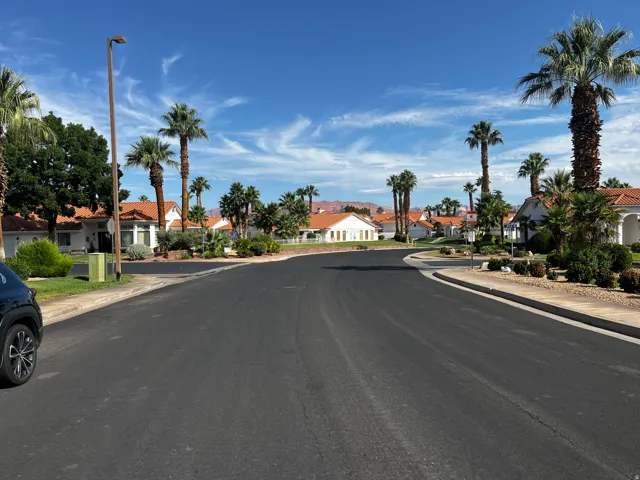 Residential street featuring Mediterranean-style homes with terra cotta roofs, mature palm trees, and desert landscaping