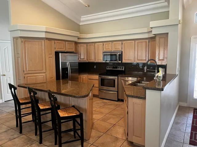 Spacious kitchen featuring light wood cabinetry, granite countertops, stainless steel appliances, a large central island, and tile flooring