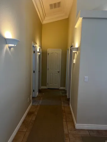 Hallway featuring tile flooring with a carpet runner, multiple doorways, and wall sconces providing ambient lighting