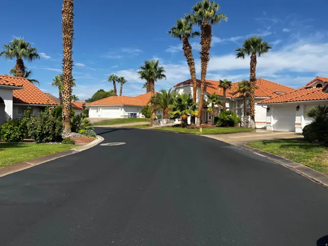 Residential street featuring mature palm trees and Mediterranean-style homes with terra cotta roof tiles, white stucco exteriors, and attached garages