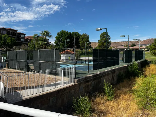 Multiple tennis courts featuring perimeter fencing and screening