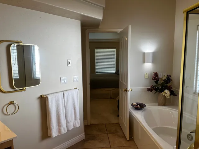 Bathroom featuring a large built-in soaking tub, a wall-mounted sconce, and tile flooring
