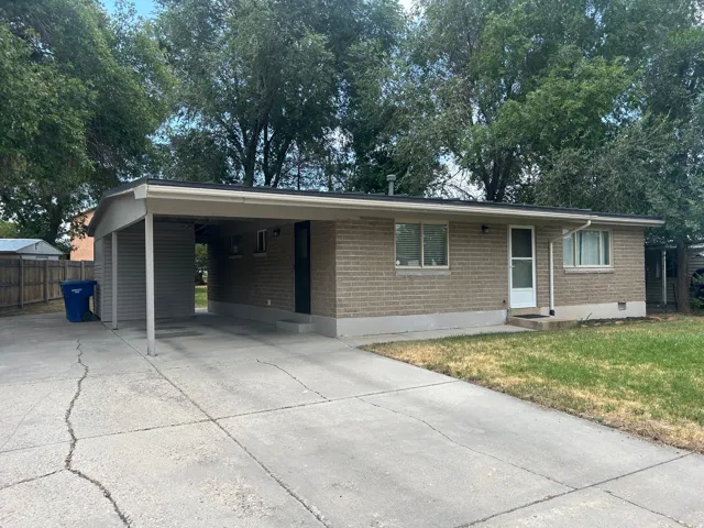 Brick exterior home featuring a covered carport, mature trees, concrete driveway, and a front lawn