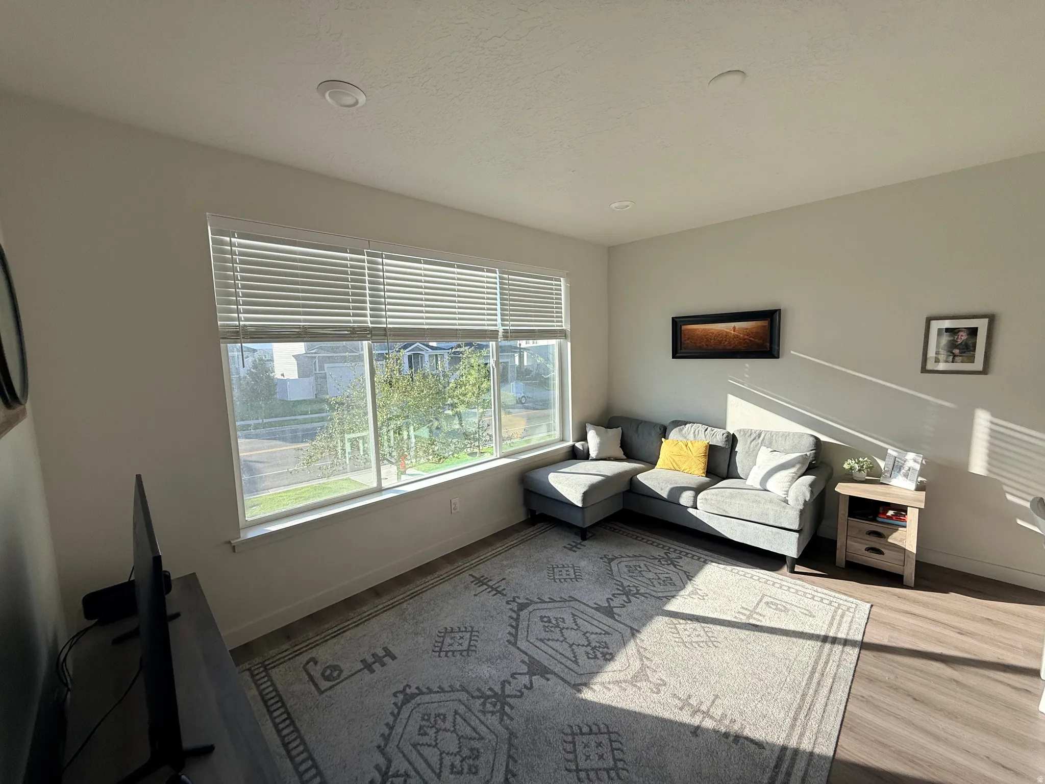 Living area featuring wood-finish flooring, recessed lighting, and a large picture window with blinds