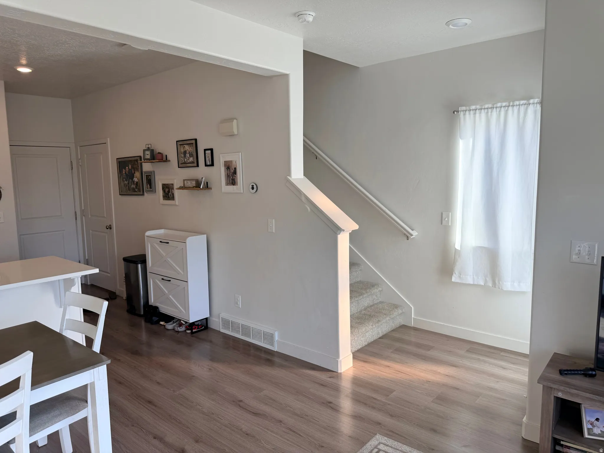 Open-concept living space with wood-finish flooring, a contemporary staircase featuring carpeted treads and white railings, and recessed lighting