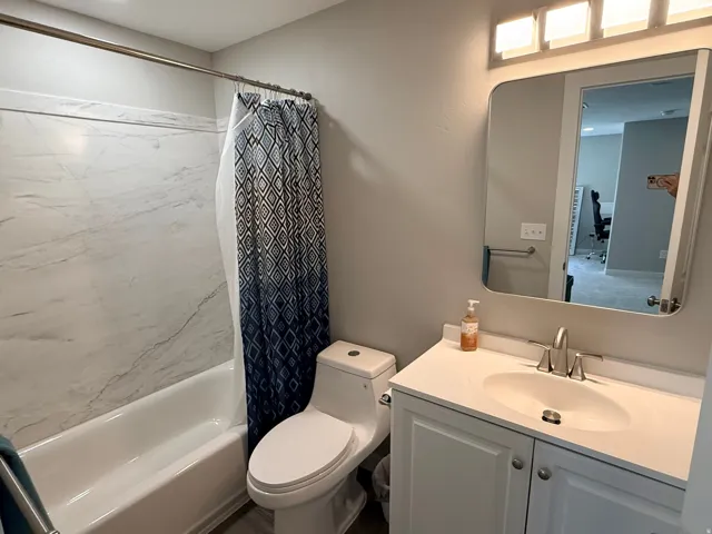 Bathroom featuring a built-in bathtub with a marble-patterned surround, a white vanity with integrated sink, brushed nickel faucet, and a contemporary rectangular mirror with integrated lighting