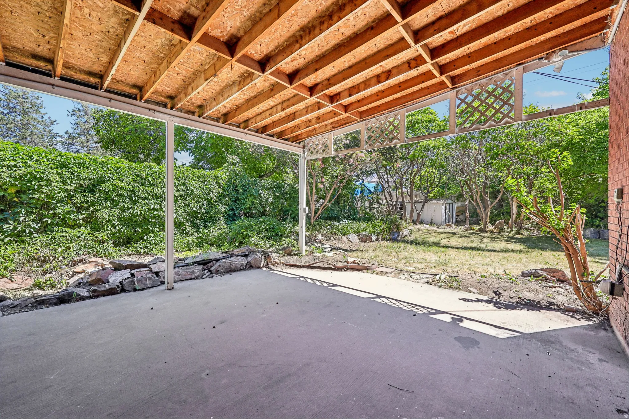 Expansive covered concrete patio featuring white support beams and an exposed wood ceiling