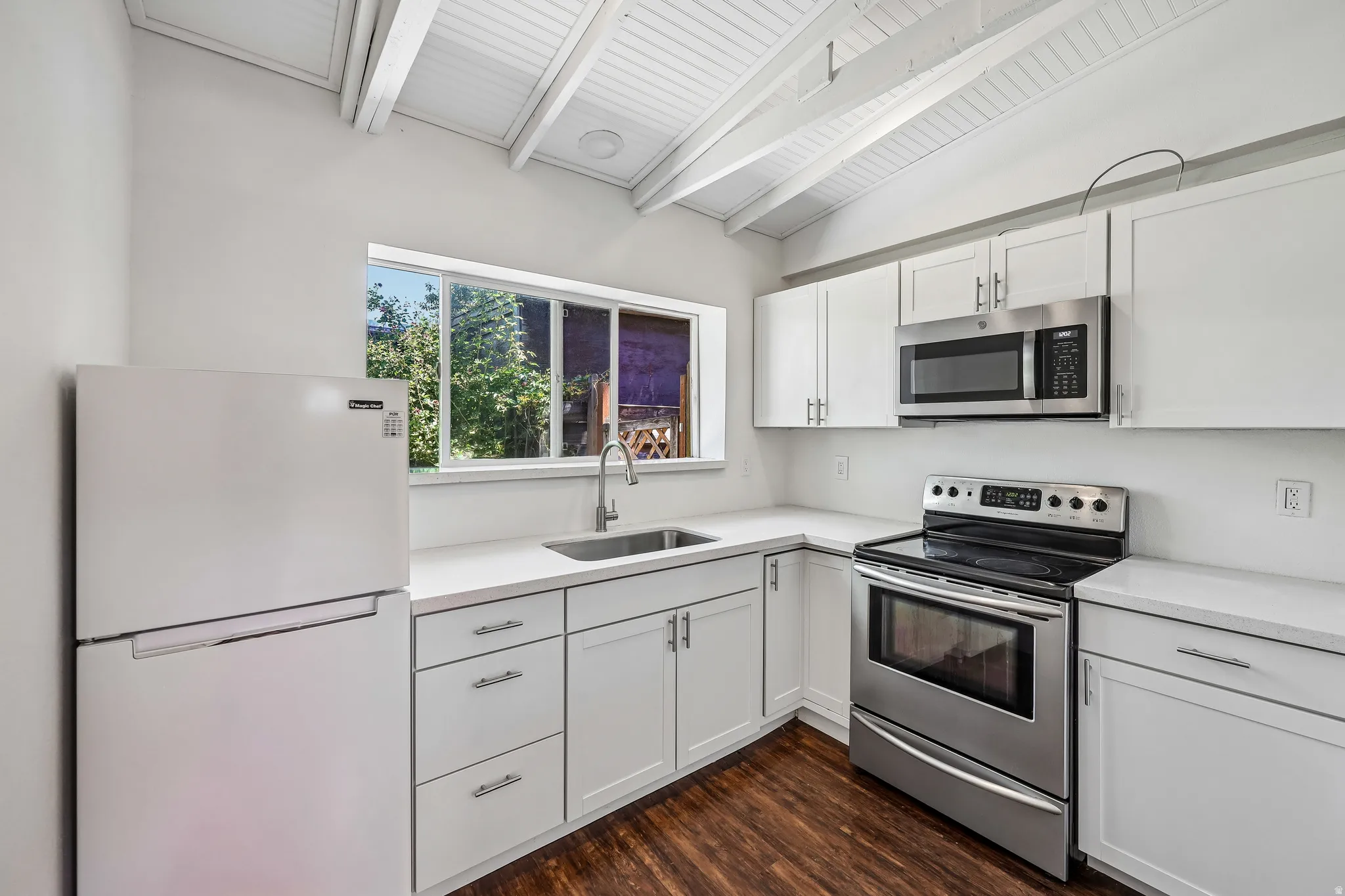 Kitchen featuring white cabinetry, light-toned countertops, stainless steel appliances, and wood-finish flooring